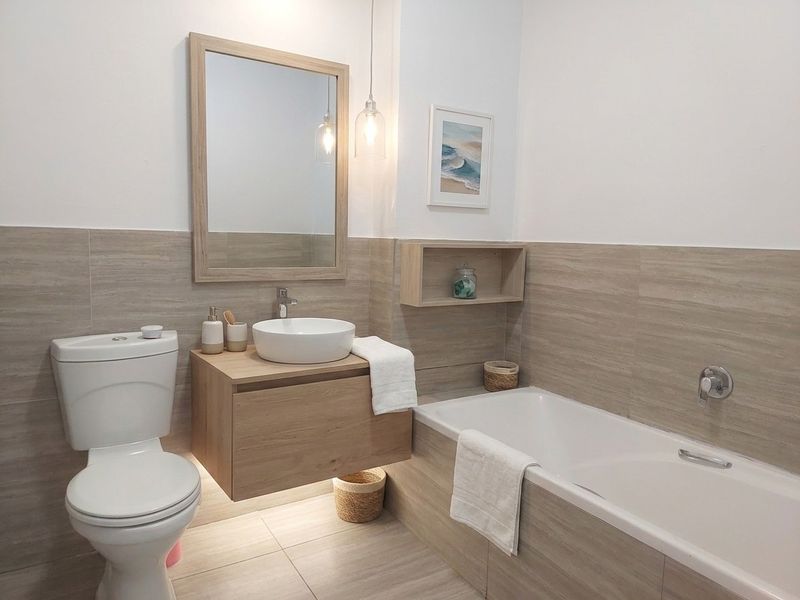 Modern bathroom featuring a wall-mounted vanity with vessel sink, built-in bathtub, and neutral-toned tiled wall finishes.