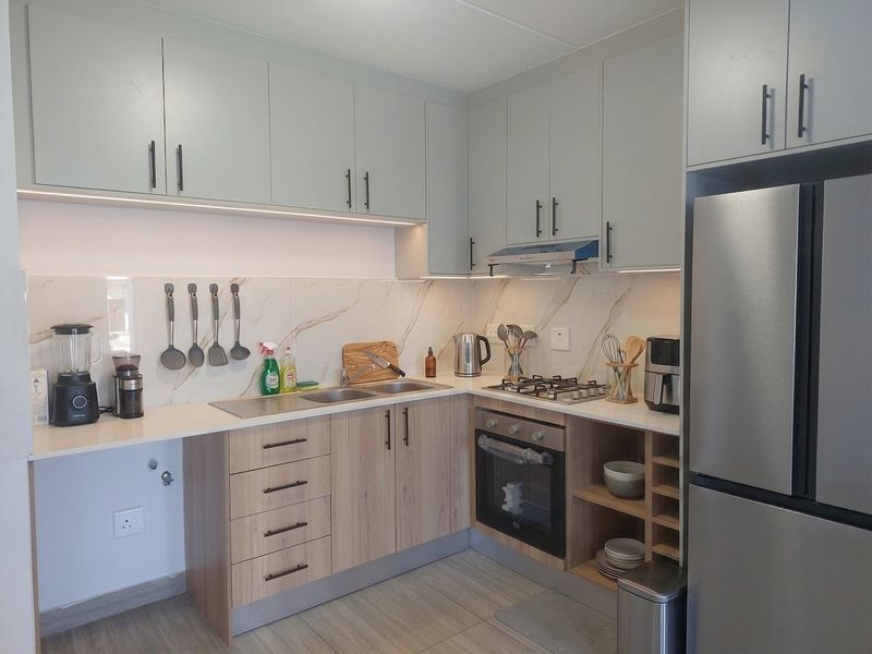 Modern kitchen featuring light wood-tone lower cabinetry, sleek grey upper cabinets, marble-look backsplash, gas hob, and integrated oven with under-cabinet lighting.