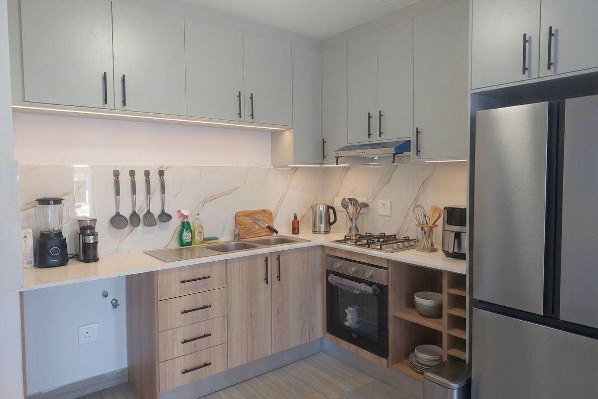 Modern kitchen featuring light wood-tone lower cabinetry, sleek grey upper cabinets, marble-look backsplash, gas hob, and integrated oven with under-cabinet lighting.
