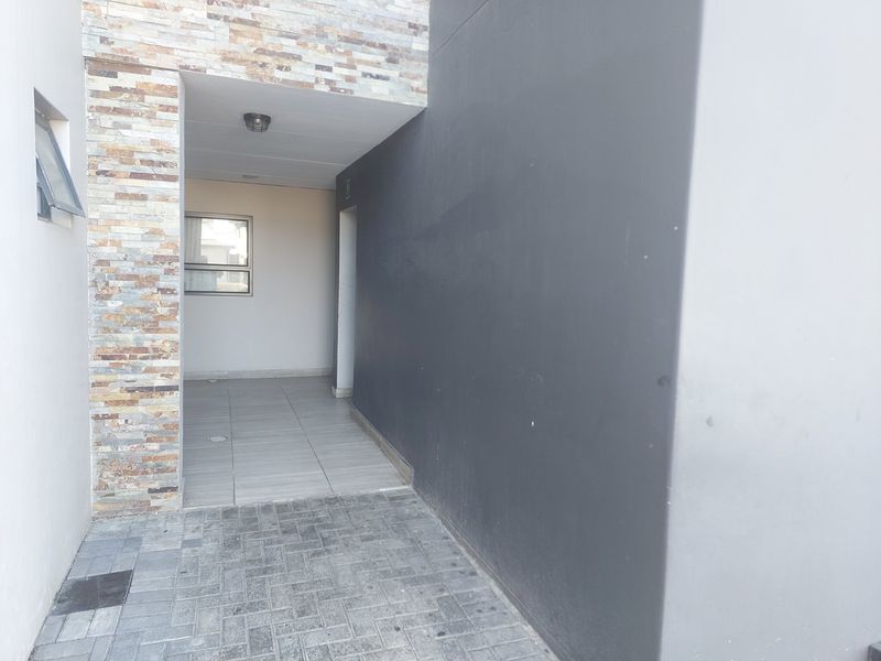 A clean exterior entrance area featuring stone cladding, paved flooring, and a covered tiled walkway leading to the front door.