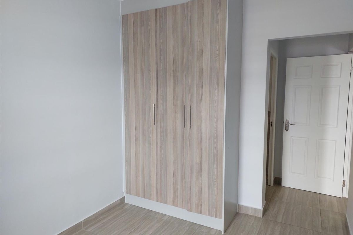 A clean, empty bedroom featuring modern wood-look built-in wardrobes and neutral tiled flooring, offering a bright and versatile living space.