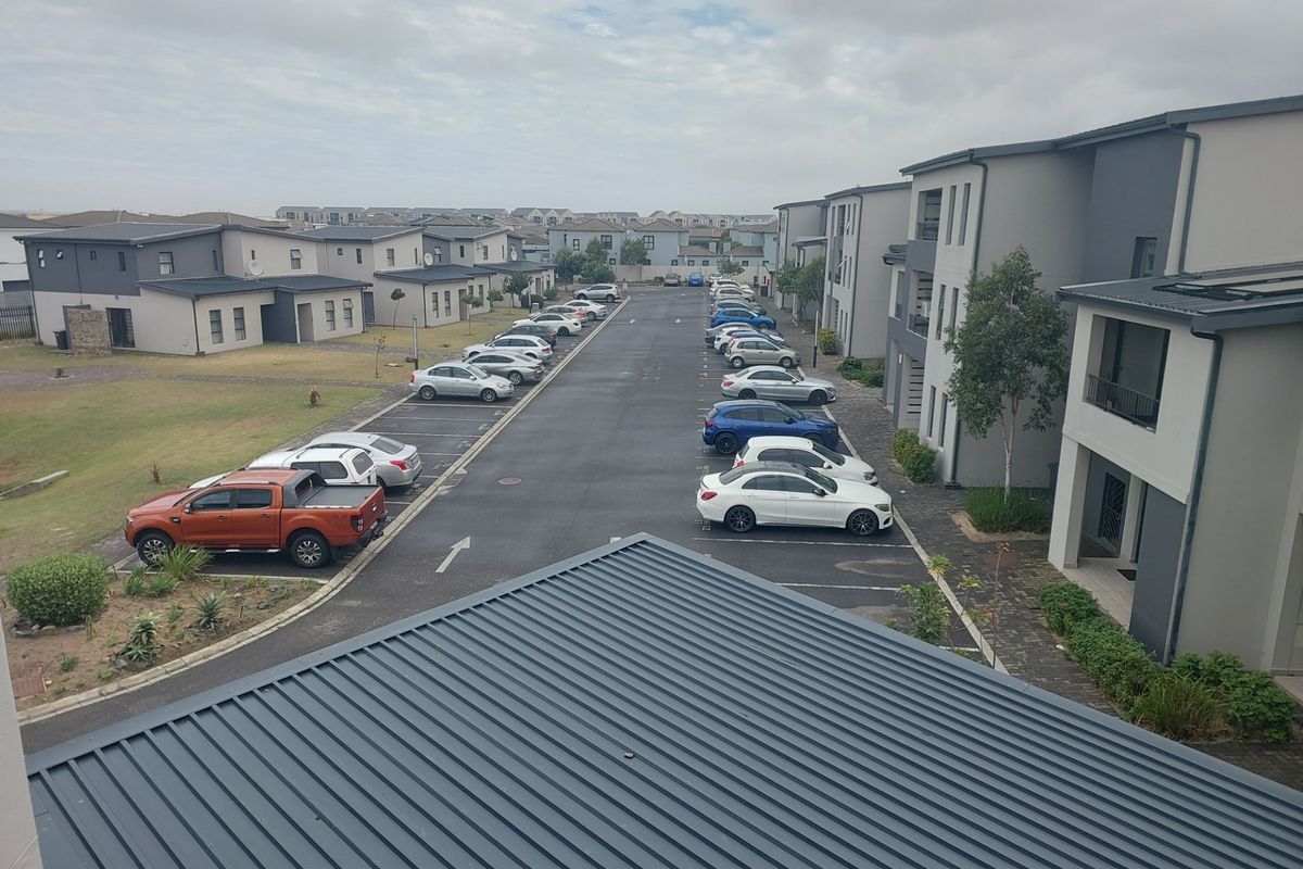 An elevated aerial view of the apartment complex parking area, featuring paved driveways, designated parking bays, and modern multi-story residential buildings.