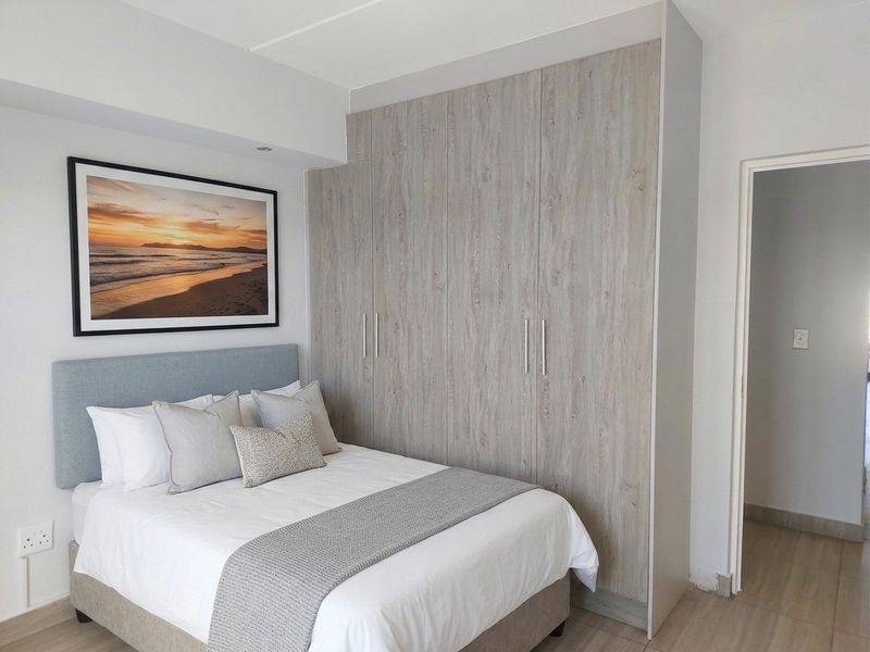 A well-maintained bedroom featuring modern wood-look built-in cupboards, neutral laminate flooring, and clean finishes.