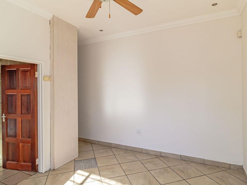 An empty bedroom featuring tiled flooring, a ceiling fan, and recessed lighting, with an adjacent en-suite bathroom visible through a wooden door.