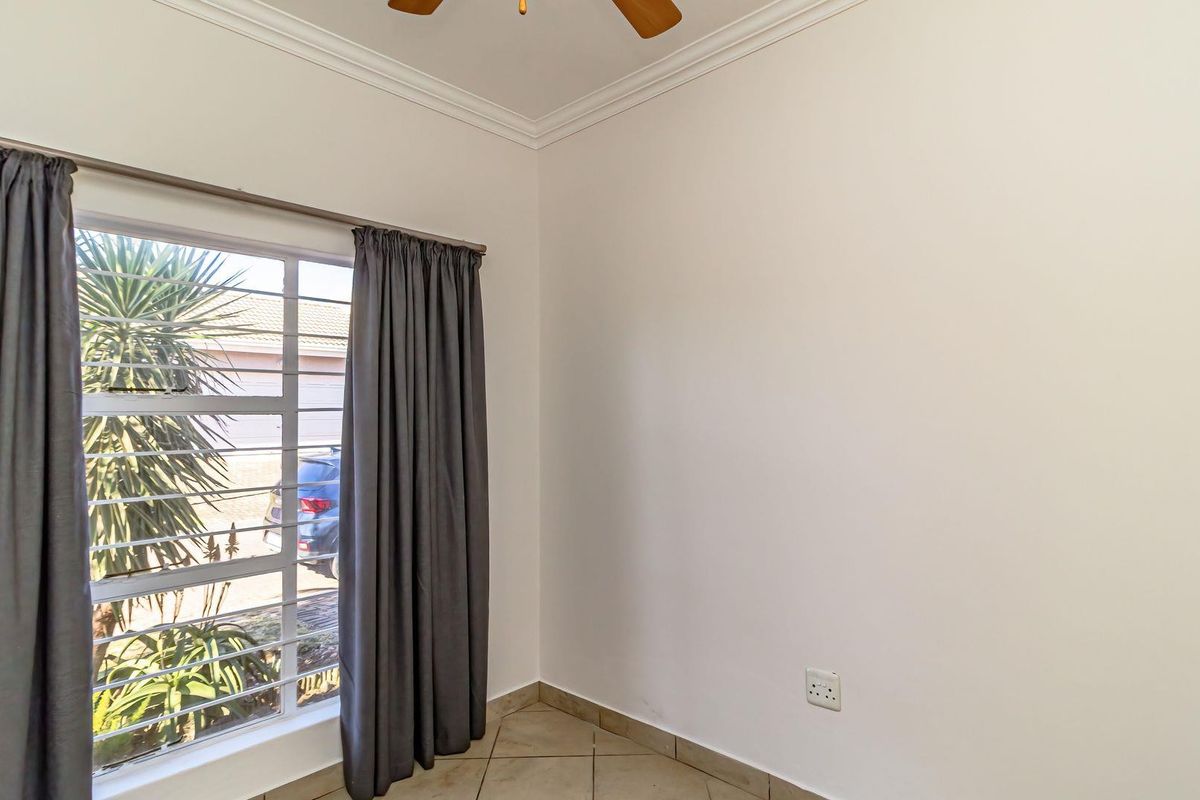 A bright, empty bedroom featuring tiled flooring, a ceiling fan, and a window fitted with security bars.