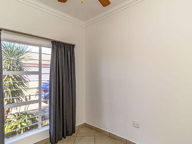 A bright, empty bedroom featuring tiled flooring, a ceiling fan, and a window fitted with security bars.
