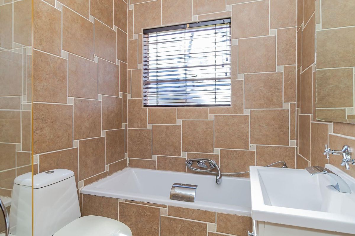 A functional bathroom featuring a built-in bathtub, wall-mounted basin, and floor-to-ceiling tiled walls with a neutral color palette.
