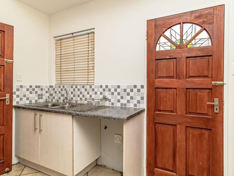A functional scullery area featuring a double sink, tiled splashback, and timber doors, providing a practical utility space for the home.
