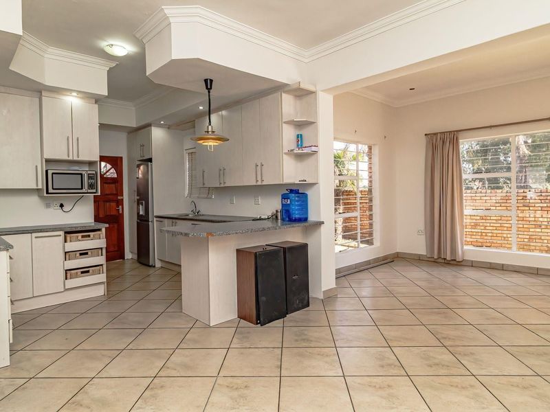 Open-plan kitchen and living area featuring light-toned cabinetry, granite countertops, ceramic tile flooring, and ample natural light through large windows.