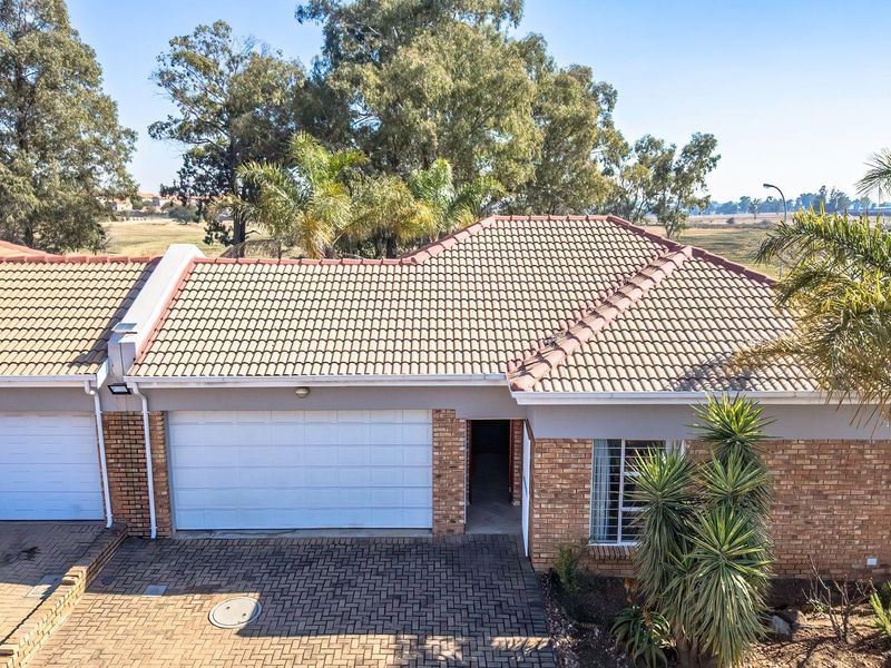 An elevated view of the front facade featuring a brick exterior, tiled roof, paved driveway, and a single garage.