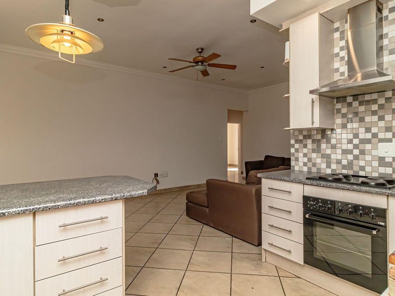 Open-plan kitchen and living area featuring tiled flooring, built-in cabinetry with granite countertops, and integrated cooking appliances.