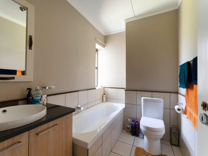 A functional bathroom featuring a vanity with a vessel sink, a bathtub, and a toilet, finished with neutral wall tiles and floor tiling.