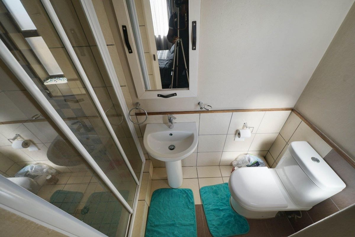 A compact bathroom featuring a pedestal washbasin, a glass-enclosed shower, and a standard toilet with neutral wall and floor tiling.
