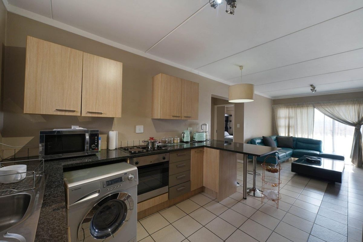 Open-plan kitchen and living area featuring light wood cabinetry, granite countertops, integrated appliances, and tiled flooring throughout the space.