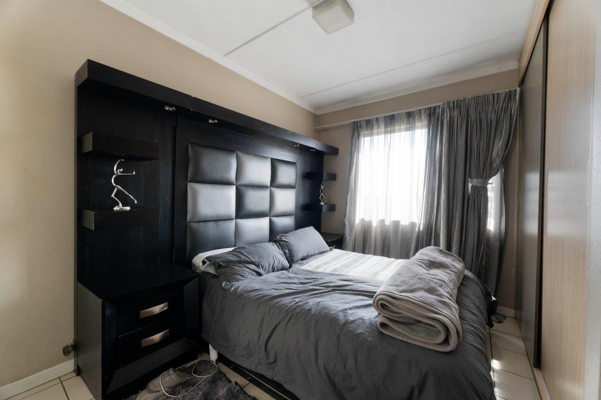 A well-maintained bedroom featuring a modern built-in headboard with integrated bedside tables and a large sliding door wardrobe.