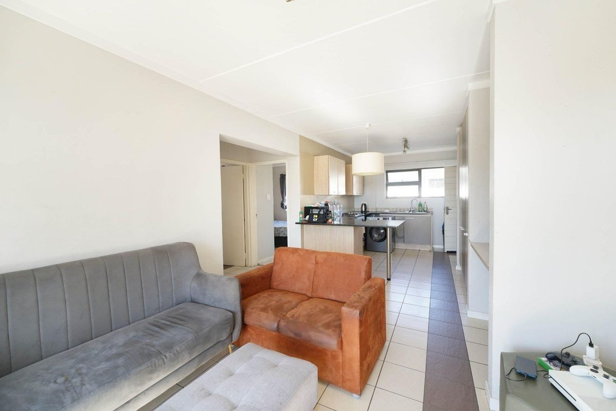 Open-plan living area featuring a functional kitchen with cabinetry, breakfast counter, and tiled flooring, seamlessly connected to the lounge space.