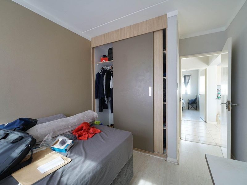 A bedroom featuring built-in sliding door wardrobes and light-toned laminate flooring, with an open doorway leading to an adjacent hallway.