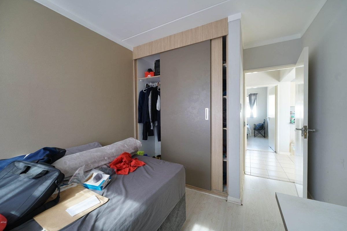 A bedroom featuring built-in sliding door wardrobes and light-toned laminate flooring, with an open doorway leading to an adjacent hallway.
