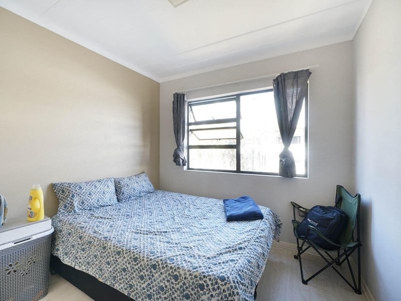 A functional bedroom featuring laminate flooring and an aluminium-framed window, providing a neutral space ready for personalization.