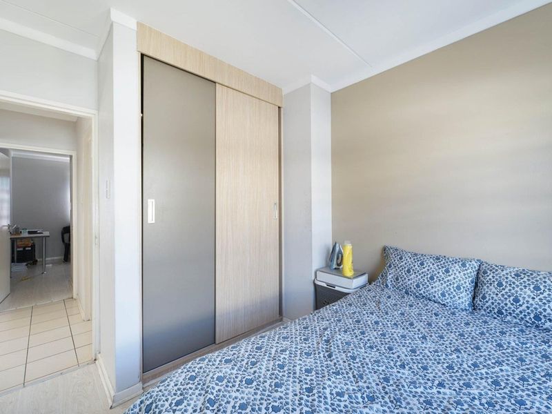 A well-maintained bedroom featuring built-in sliding door wardrobes, neutral wall finishes, and tiled flooring, with an adjacent hallway visible.