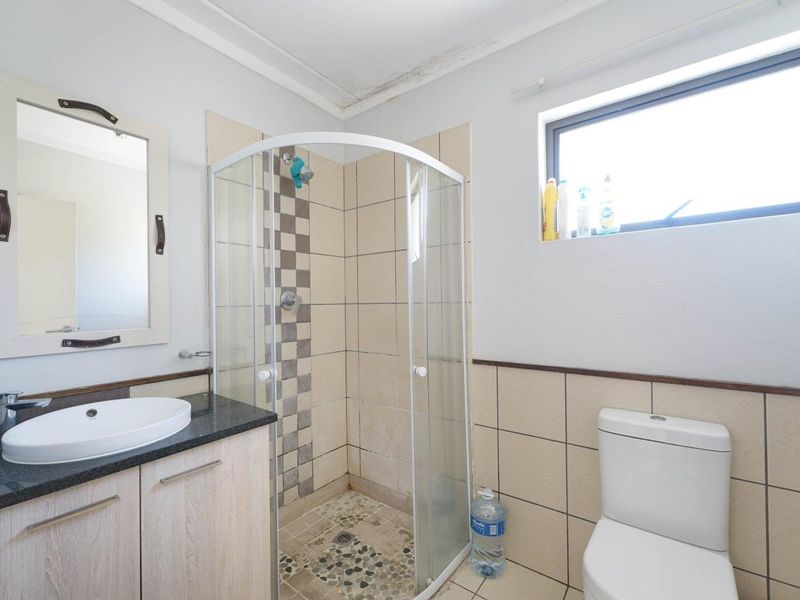 A functional bathroom featuring a corner shower enclosure, vanity with countertop basin, and toilet, with visible water staining on the ceiling requiring attention.