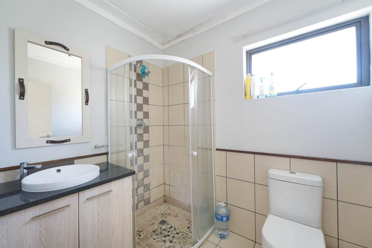 A functional bathroom featuring a corner shower enclosure, vanity with countertop basin, and toilet, with visible water staining on the ceiling requiring attention.