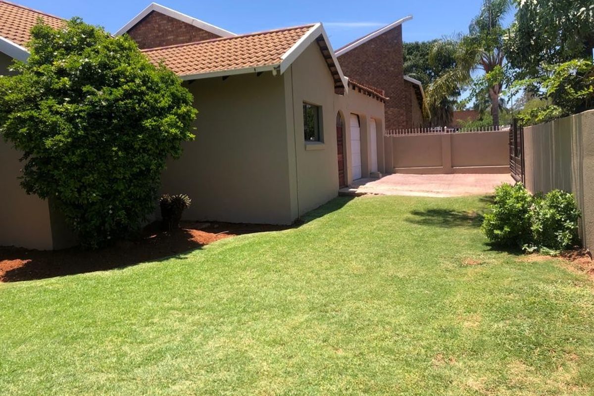 A view of the rear exterior of the house featuring a well-maintained lawn, paved driveway area, and brick boundary wall.