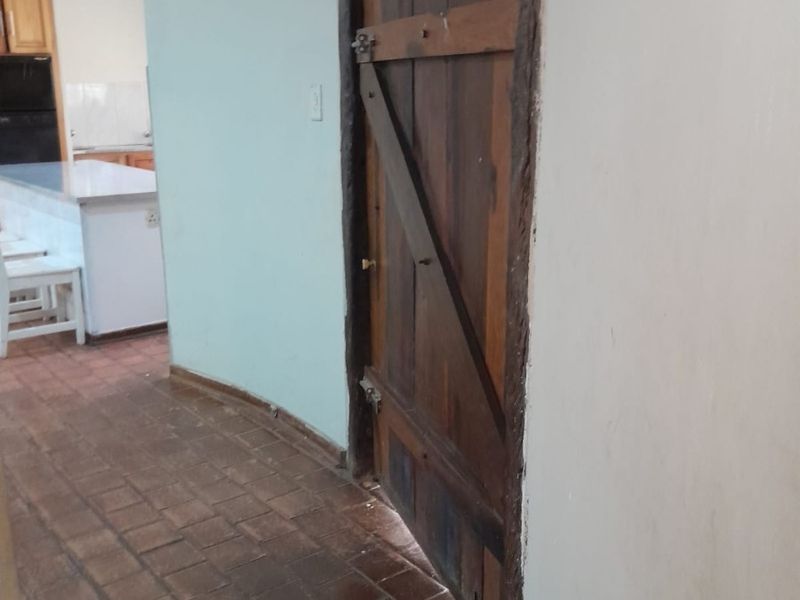 A hallway featuring rustic timber door and terracotta tile flooring, leading into an open-plan kitchen area.