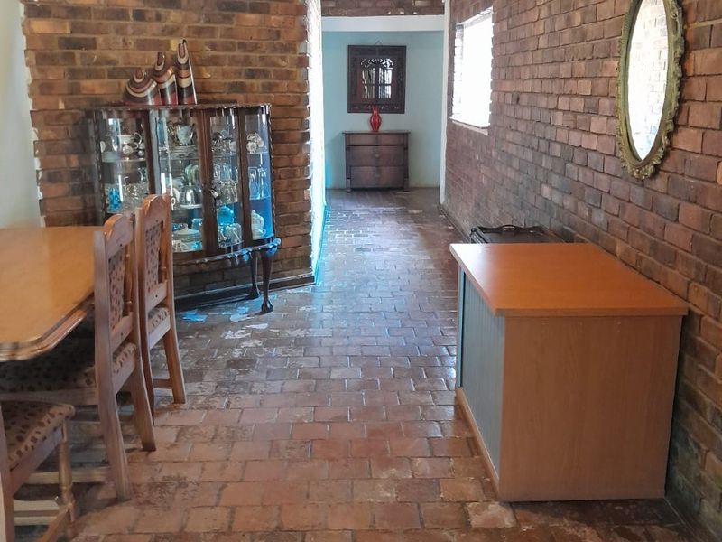 Dining area featuring rustic exposed brick walls and traditional terracotta tile flooring, leading into a hallway space.