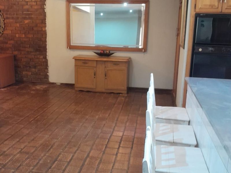 Open plan kitchen and living area featuring terracotta tile flooring, exposed brick feature wall, and built-in kitchen cabinetry with integrated appliances.