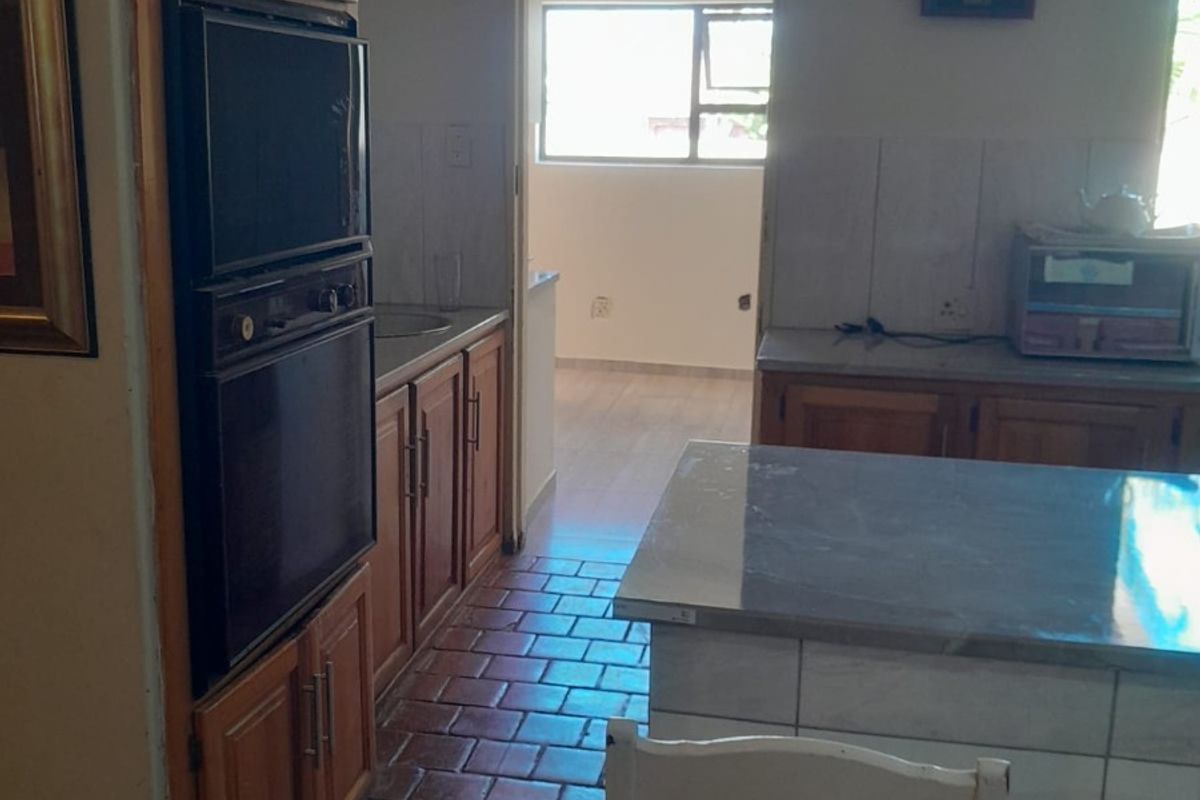 A functional kitchen featuring wooden cabinetry, a built-in oven, tiled countertops, and a central island, with direct access to an adjacent room.
