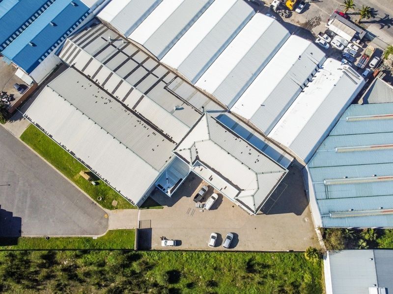 Aerial view of an industrial property complex featuring multiple warehouse buildings with metal roofing and paved parking areas.