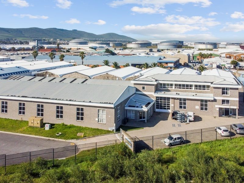 Aerial view of an industrial property featuring a large warehouse complex with metal roofing, brick facade, and secure perimeter fencing in an industrial park.