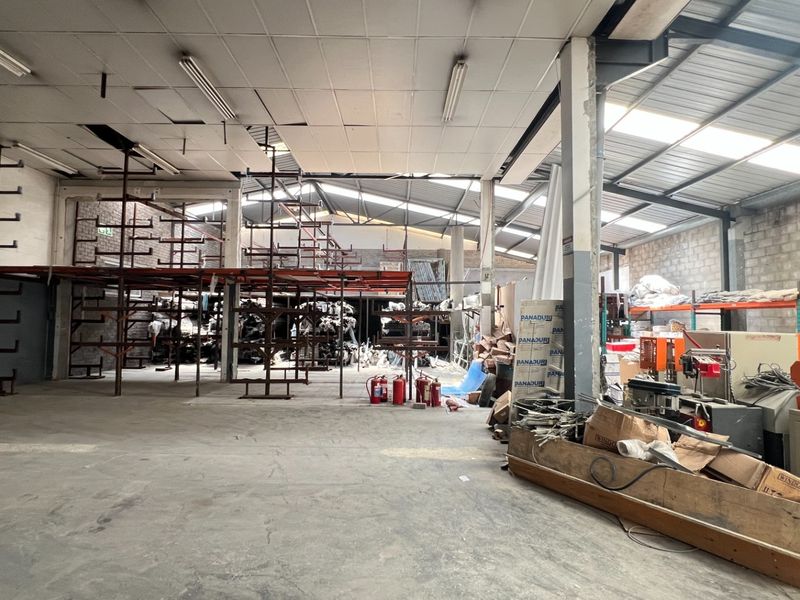 Spacious industrial warehouse area featuring concrete flooring, exposed brick walls, integrated shelving units, and functional overhead fluorescent lighting.