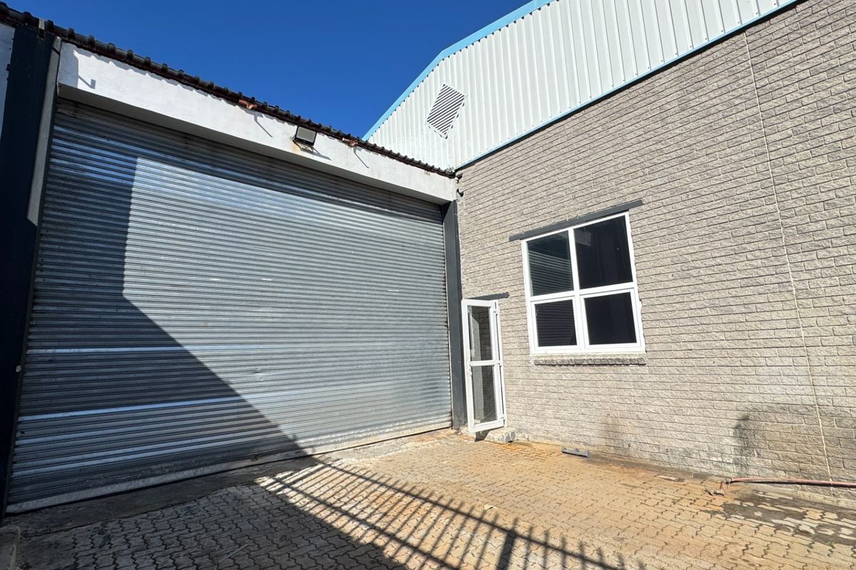 Rear exterior view of an industrial property featuring a large roller shutter door, brick facade, and paved yard area.