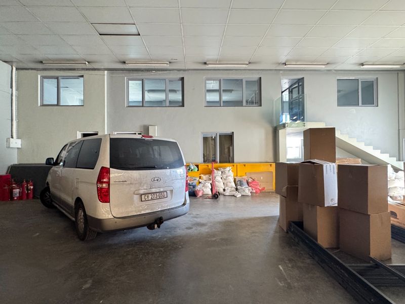 Spacious industrial garage area featuring concrete flooring, suspended ceiling with integrated lighting, and a staircase with a modern glass balustrade.