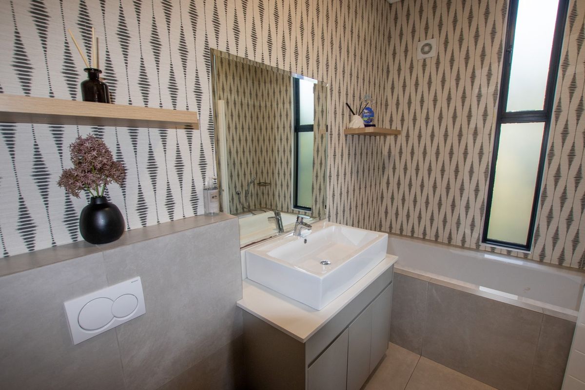 Modern bathroom featuring a vanity with basin, bathtub, wall-mounted mirror, and patterned wallpaper, providing a contemporary and functional space.