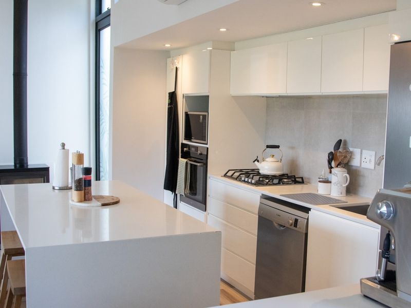 Modern kitchen featuring a central island, stone countertops, built-in appliances, and an adjacent wood-burning fireplace in an open-plan layout.