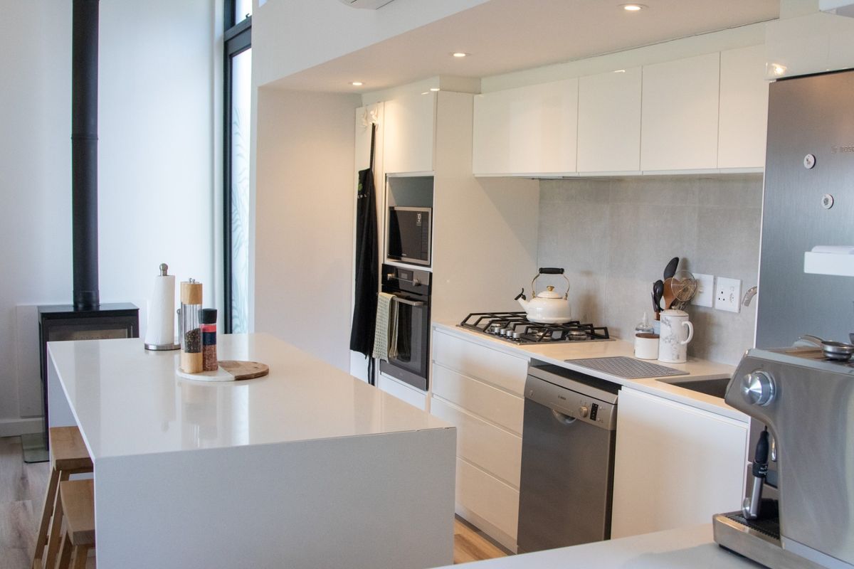 Modern kitchen featuring a central island, stone countertops, built-in appliances, and an adjacent wood-burning fireplace in an open-plan layout.