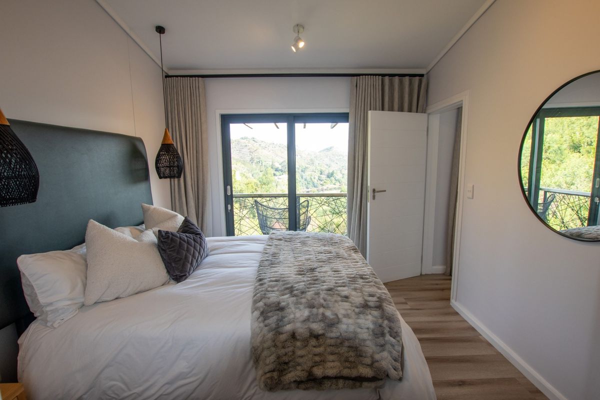 A well-maintained bedroom featuring laminate flooring, modern lighting, and a sliding glass door that opens onto a balcony with scenic views.