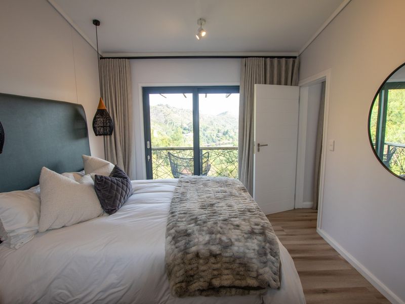 A well-maintained bedroom featuring laminate flooring, modern lighting, and a sliding glass door that opens onto a balcony with scenic views.