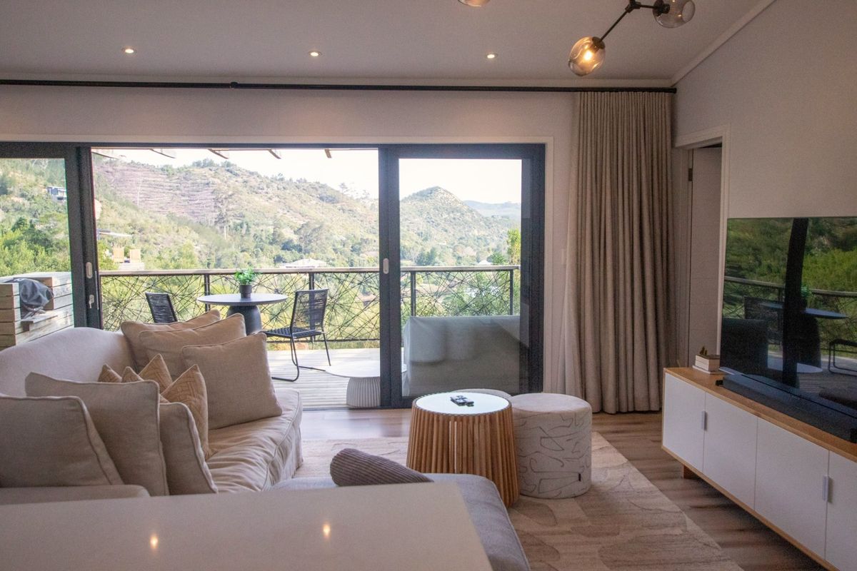 Modern living room featuring hardwood floors, recessed lighting, and large sliding glass doors opening onto a timber deck with scenic mountain views.