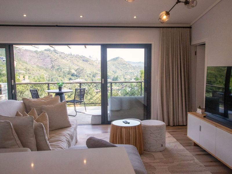 Modern living room featuring hardwood floors, recessed lighting, and large sliding glass doors opening onto a timber deck with scenic mountain views.