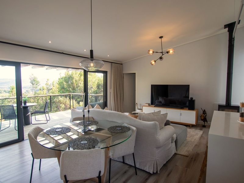 Spacious open-plan living area featuring a wood-burning fireplace, modern laminate flooring, and large sliding doors opening onto a scenic deck.