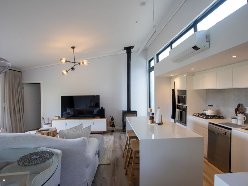 Modern open-plan living area featuring a sleek kitchen with island, wood-burning fireplace, and high-level windows providing excellent natural light.