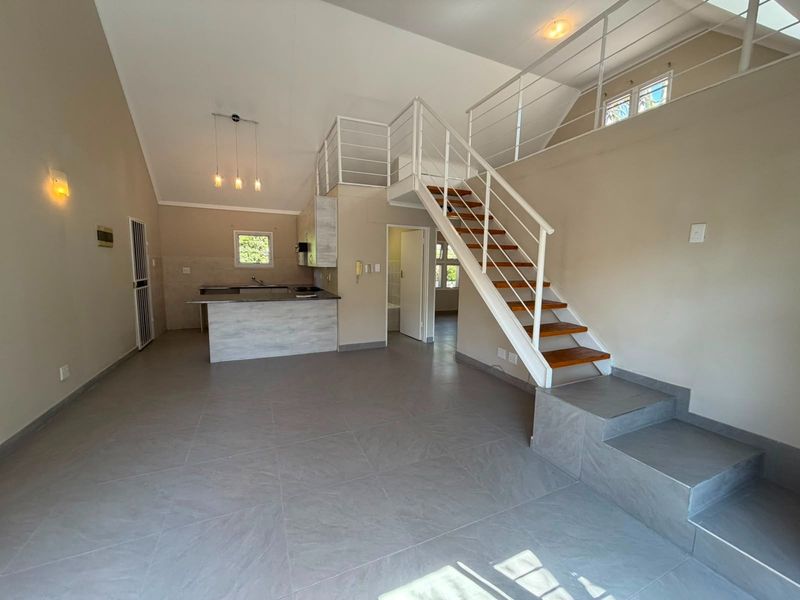 Spacious open-plan living area featuring a modern kitchen, tiled flooring, and a staircase leading to a mezzanine level.