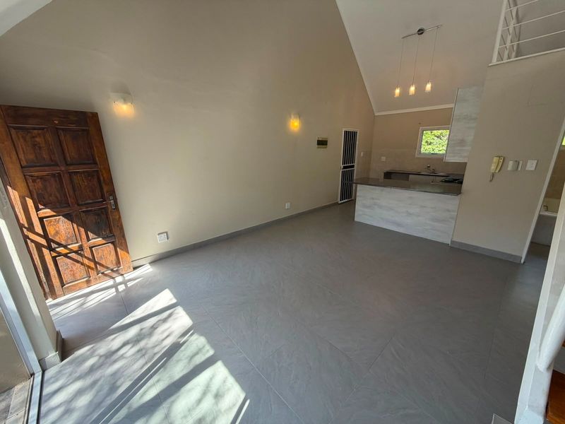 Spacious open-plan living area featuring vaulted ceilings, tiled flooring, and a functional kitchen with a breakfast island and modern lighting.