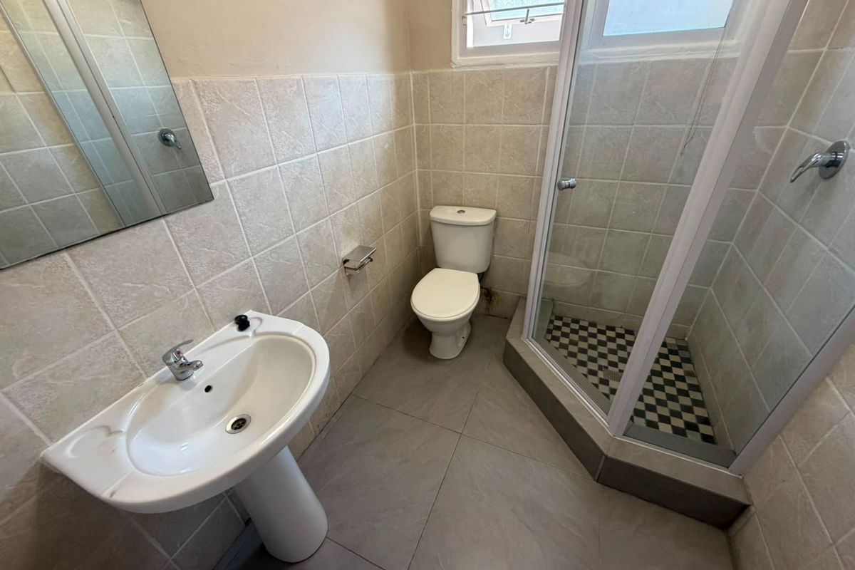 A functional bathroom featuring a pedestal basin, toilet, and a corner shower enclosure with tiled finishes throughout.