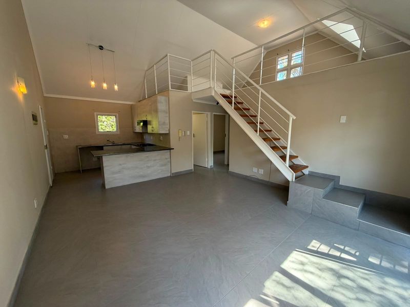 Spacious open-plan living area featuring a modern kitchen with granite countertops, tiled flooring, and a staircase leading to a mezzanine level.