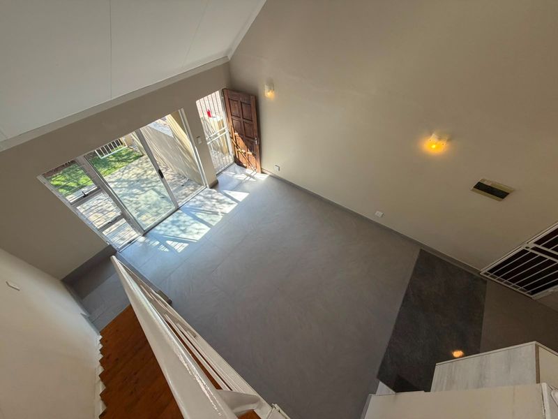 Spacious open-plan living area featuring a high vaulted ceiling, tiled floors, and direct access to an outdoor patio through sliding glass doors.